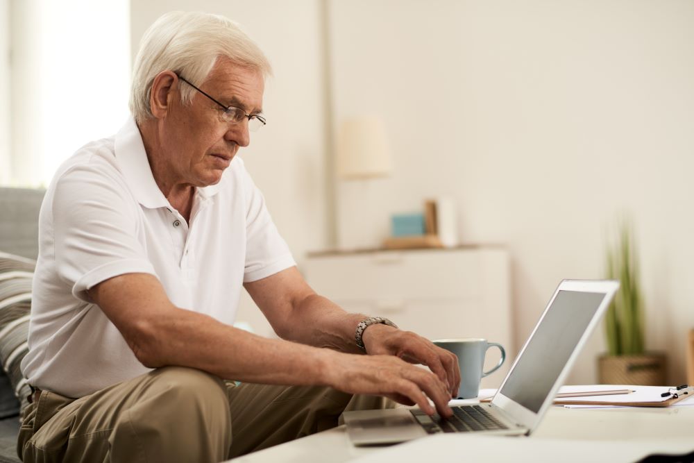 mature man at table using laptop while taking the Do I Have Hearing Loss Questionnaire
