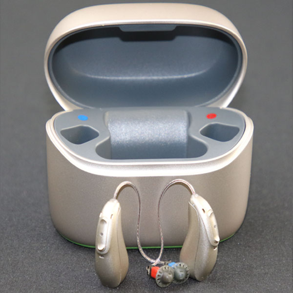 Metallic silver Phonak hearing aids stand on a gray background in front of their open charging case. 