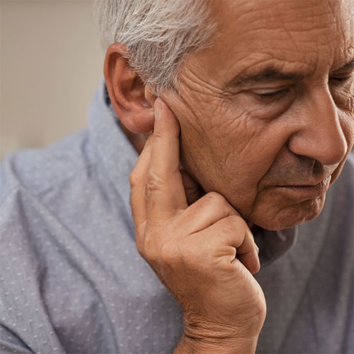 A frustrated man in his 70s holds his fingers to his ear as he struggles with hearing loss.