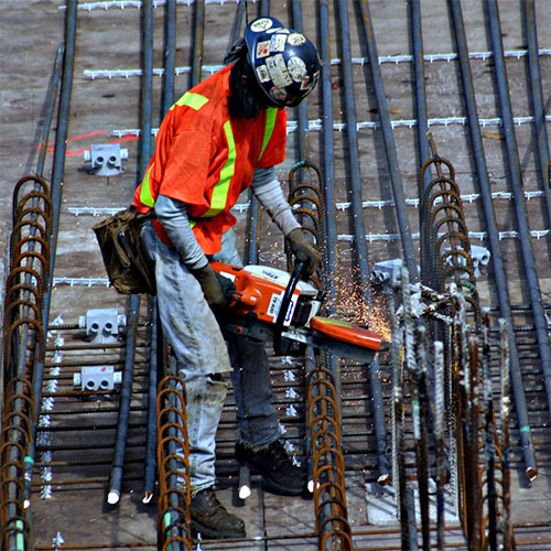 A construction worker uses a loud hand-held machine to work on rebar.