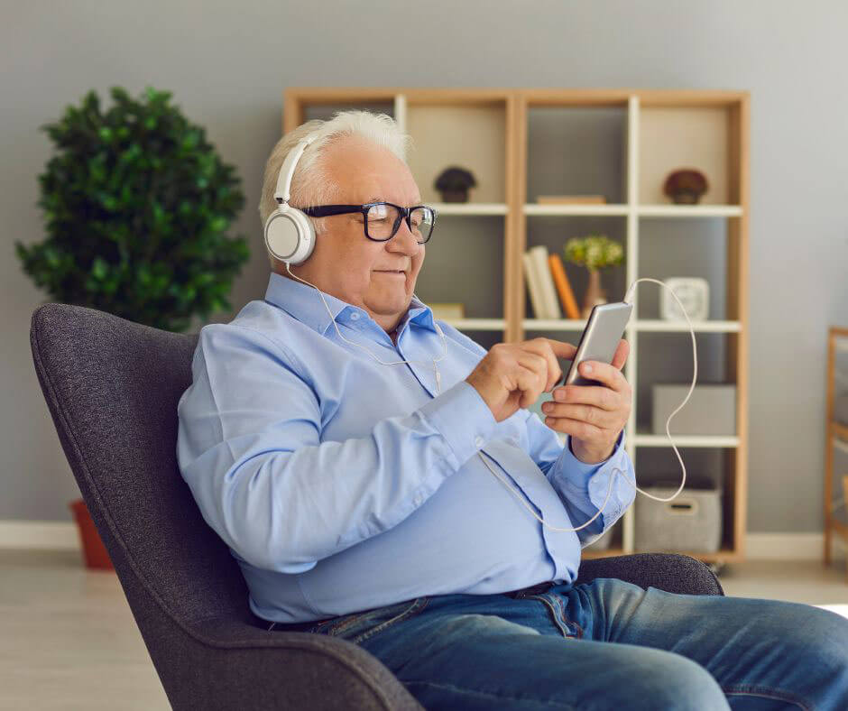 An older man wears headphones and looks at his smartphone. 