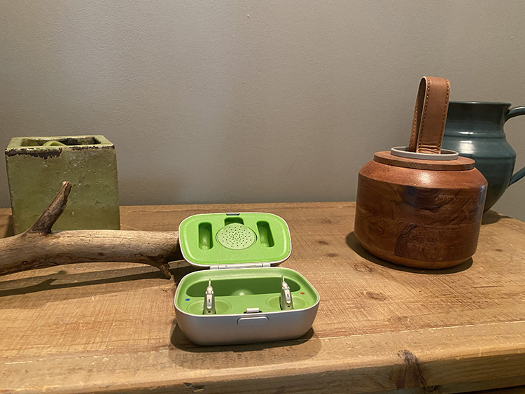 Phonak open-fit hearing aids rest in their charging case on a wooden hall table.