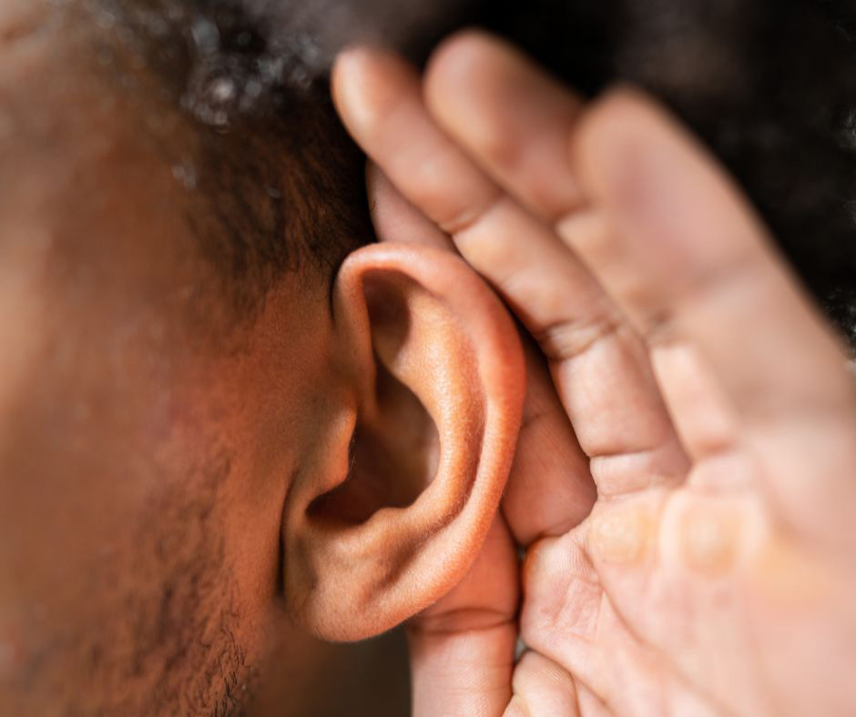 A man’s hand cups his ear as though he’s straining to hear.