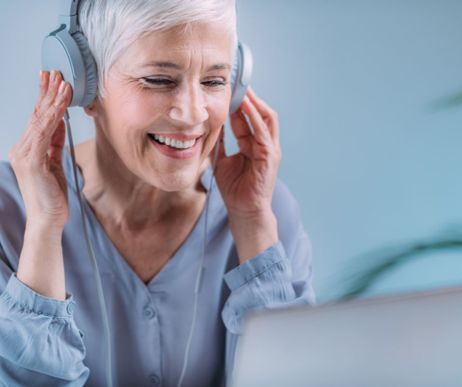 An older woman wears headphones and looks at a laptop. 