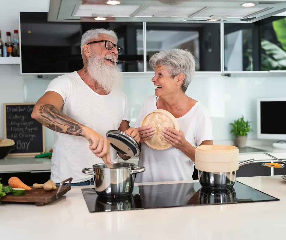 An older couple laughs while they cook together.