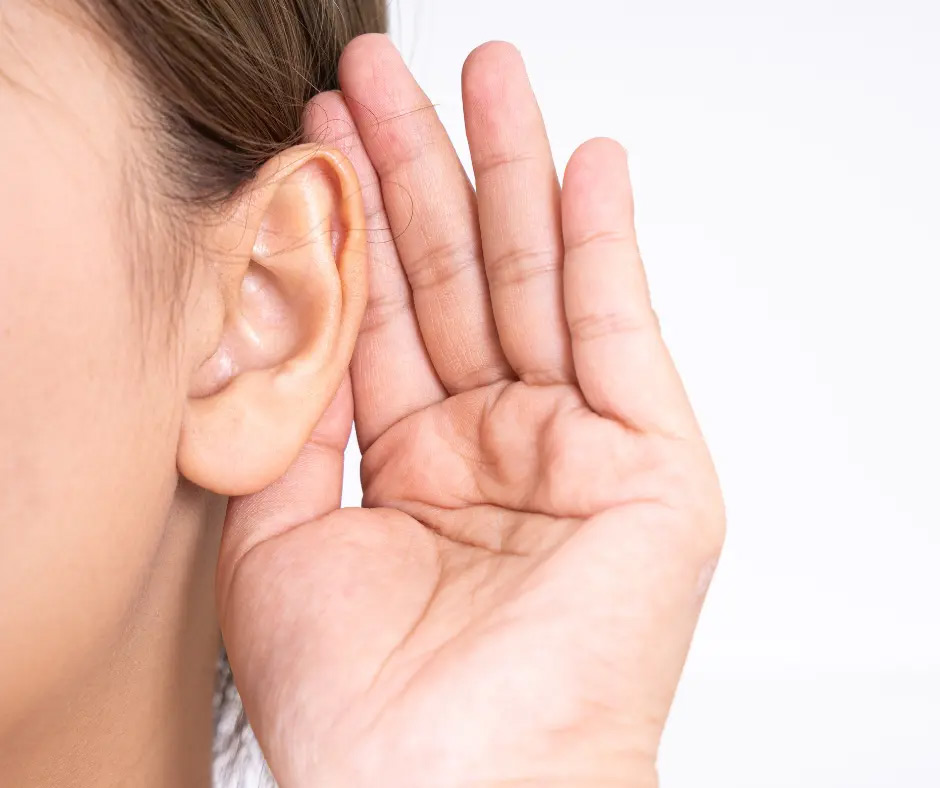 A hand cups an ear to improve hearing.