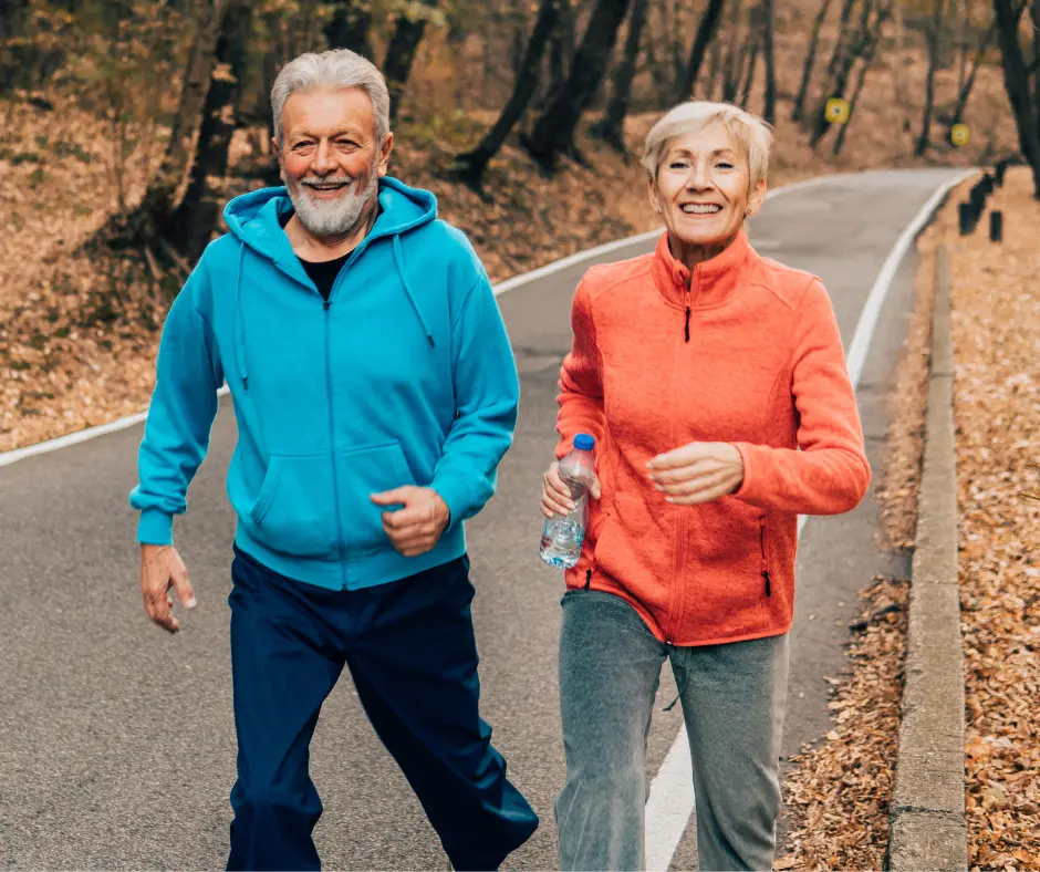 An older couple jogs on a trail during fall. 