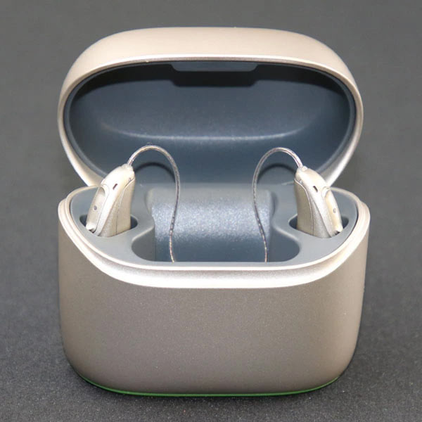 Phonak hearing aids rest in their charging case on a gray background. 
