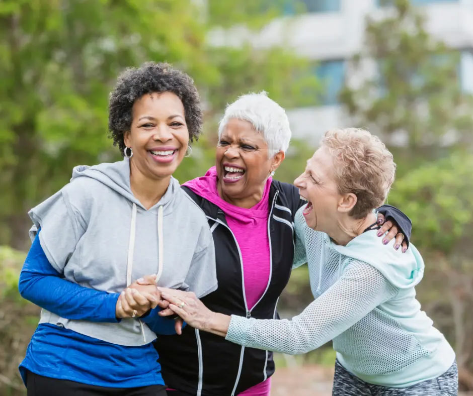Three older friends laugh together while exercising outside.