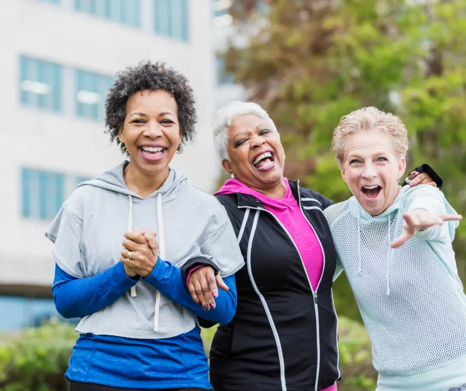 Three older women in workout gear laugh together. 