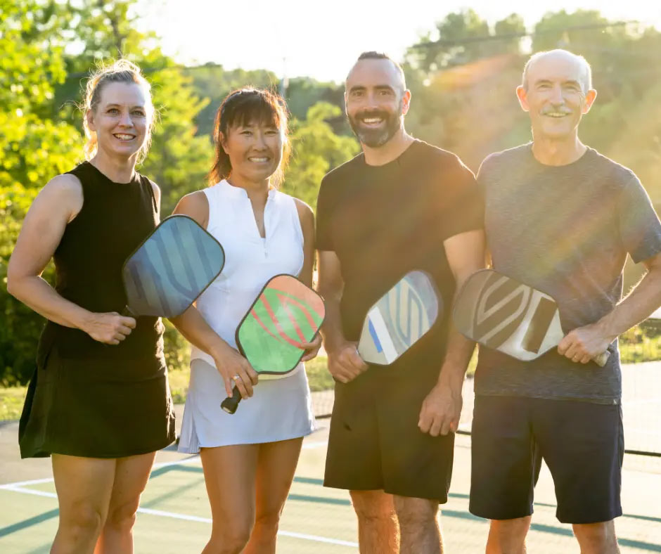 Four smiling people pose on a pickleball court.
