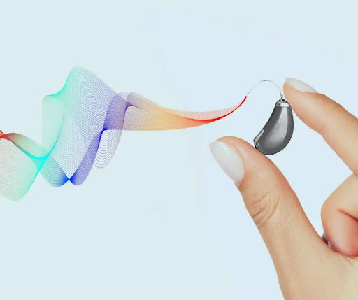 A hand holds a hearing aid with sound waves coming out of it.