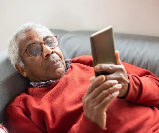 An older man looks at his phone while reclining on his couch. 